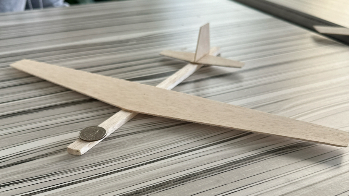 The actual balsa-wood glider, wing and boom crossed on a table with a coin for scale.